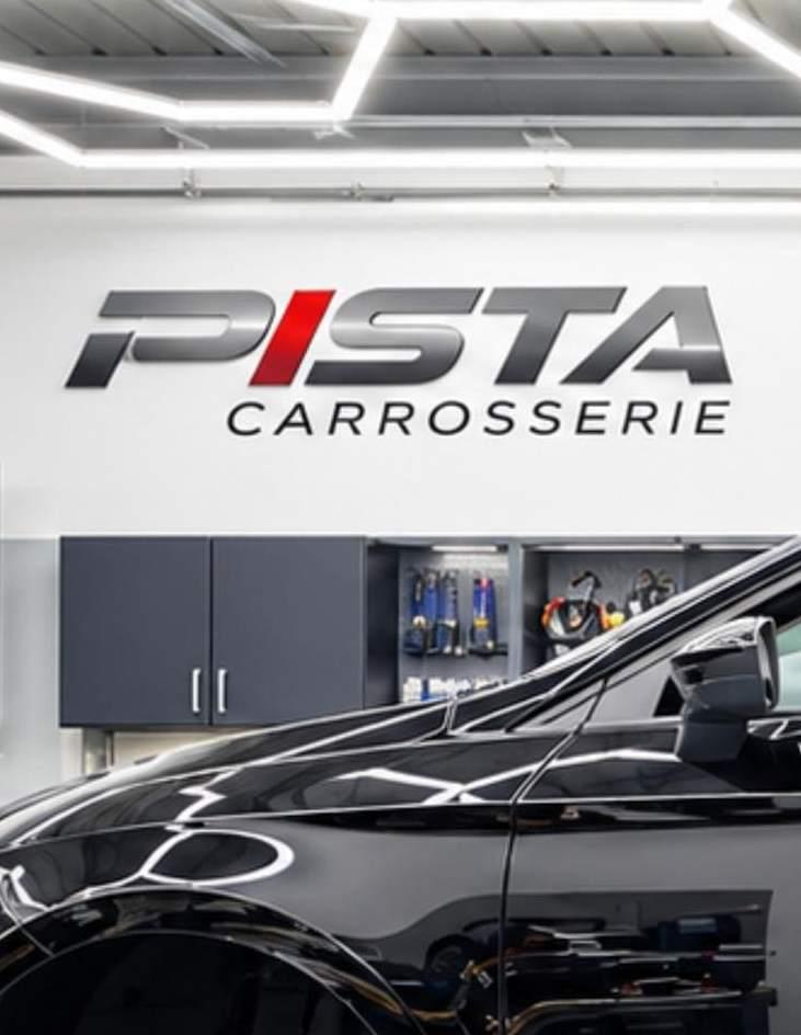 Atelier de Carrosserie Pista : plafond lumineux hexagonal, logo Pista au mur et véhicule sur pont élévateur