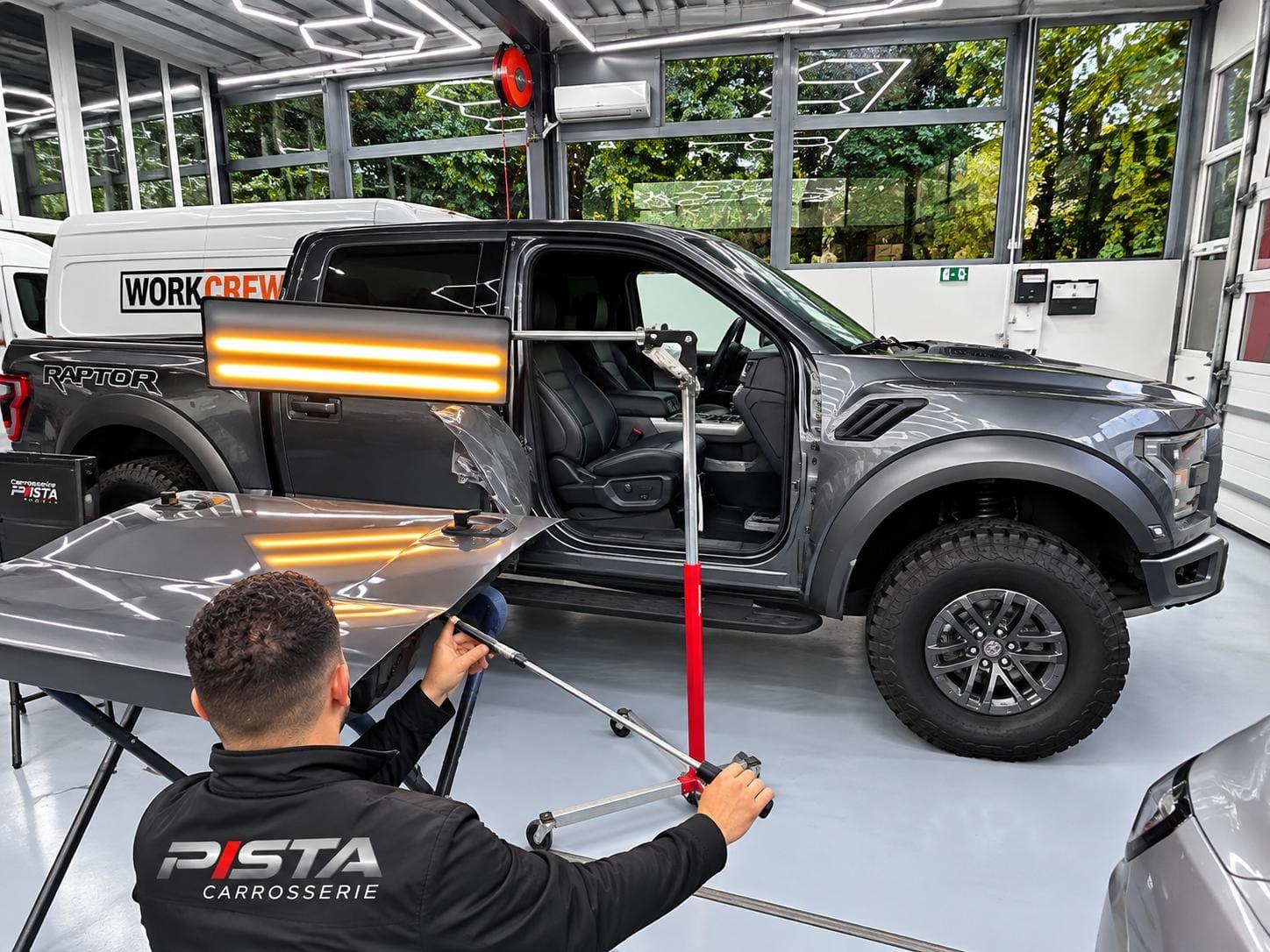 Technicien de Carrosserie Pista débosselant un panneau de carrosserie sous une lampe de contrôle